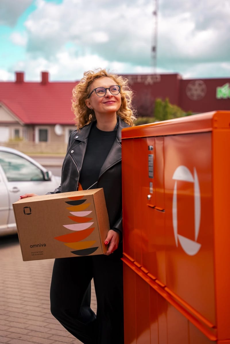 A smiling customer holding an Omniva parcel next to a parcel machine